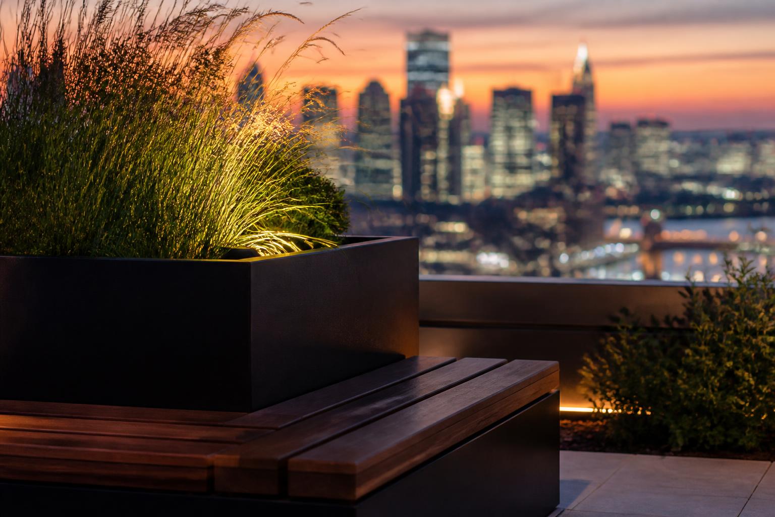 Bespoke matte black steel planter with integrated hardwood bench seat and city skyline at twilight